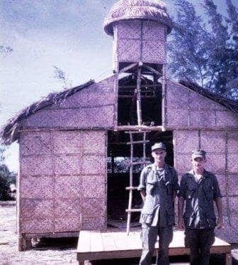 Father Capodanno (left) stands outside his makeshift chapel in Vietnam.